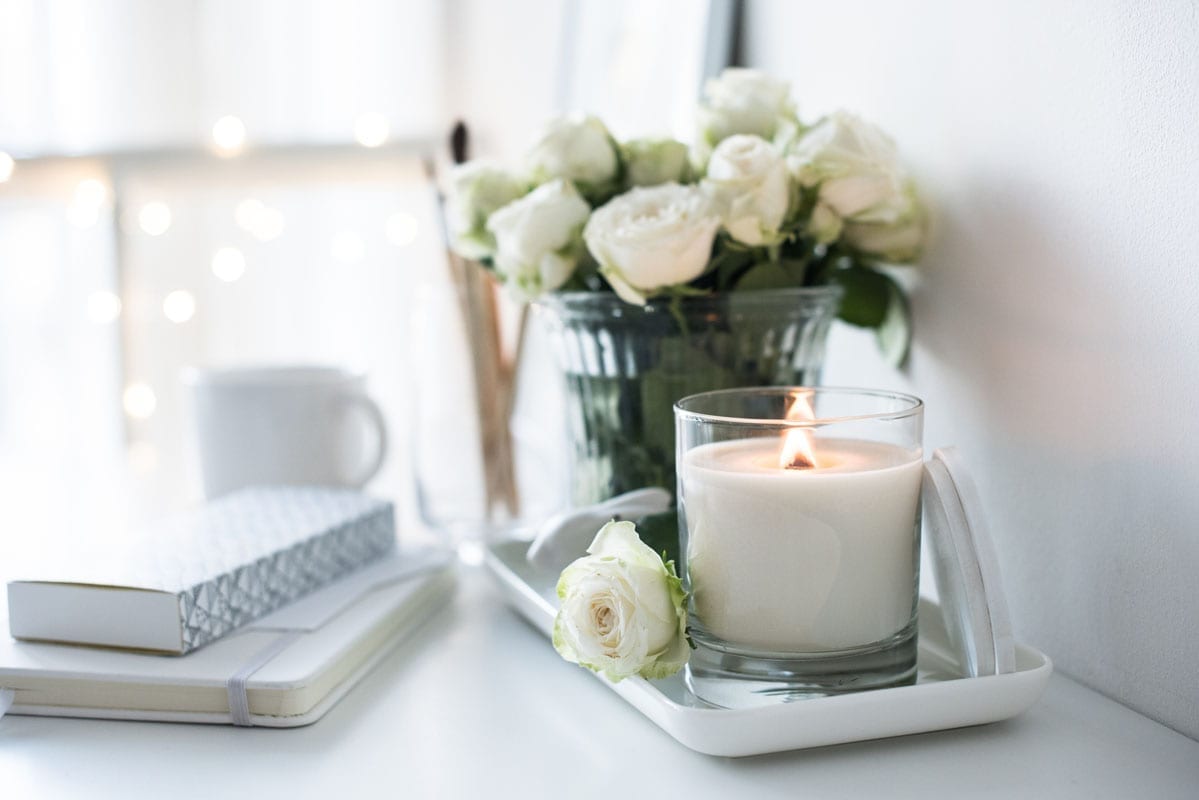 White room interior decor with burning hand-made candle and bouquet