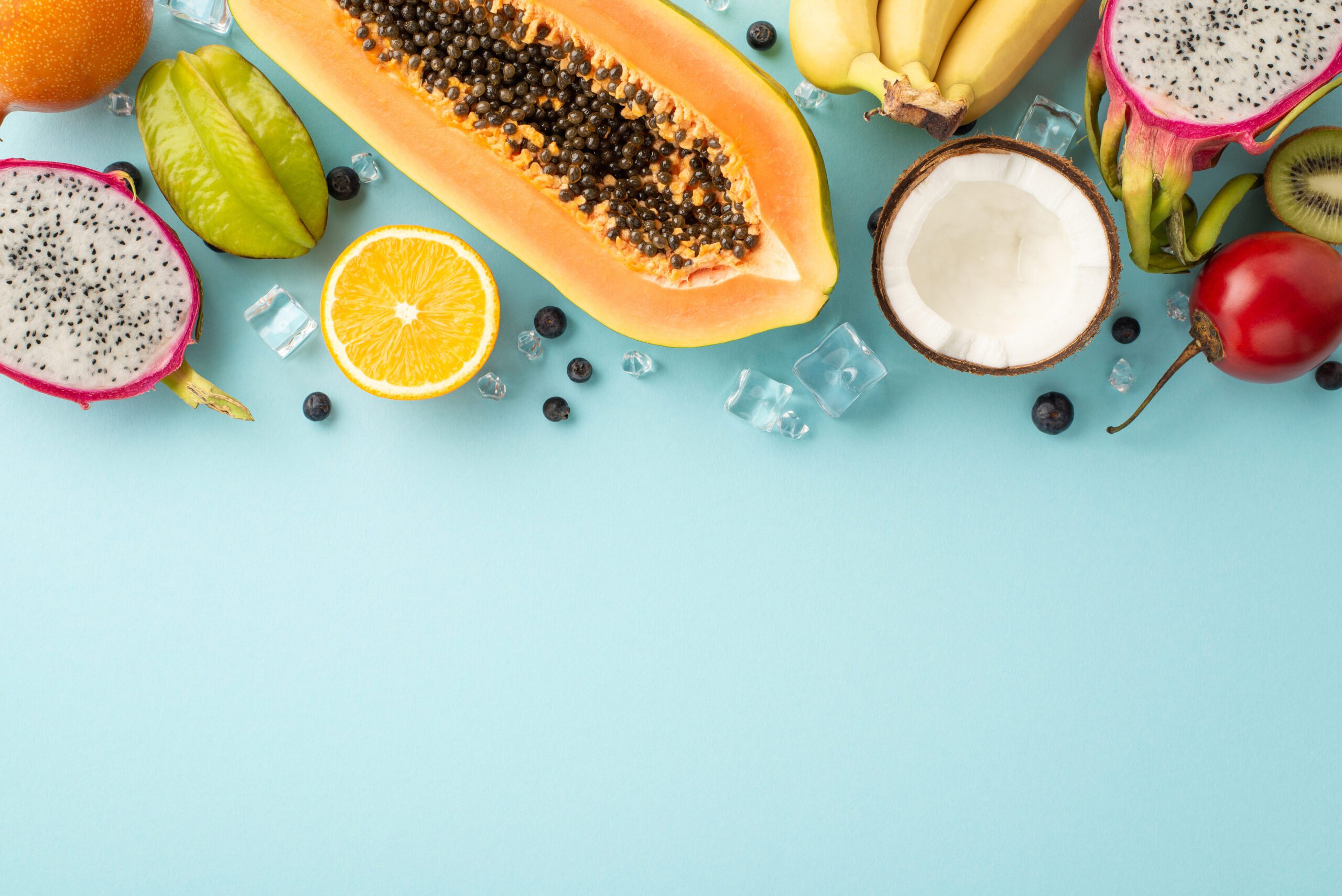 Tropical delight concept. Top view of fresh exotic dragon fruit, tomarillo, papaya, orange, carambola and coconut with on a pastel blue background with an empty space for marketing